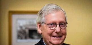 Smiling man in suit with round glasses indoors.