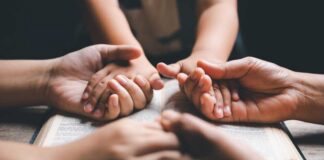 Multiple hands clasped together over an open book