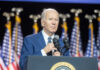 Man speaking at podium with flags behind him.
