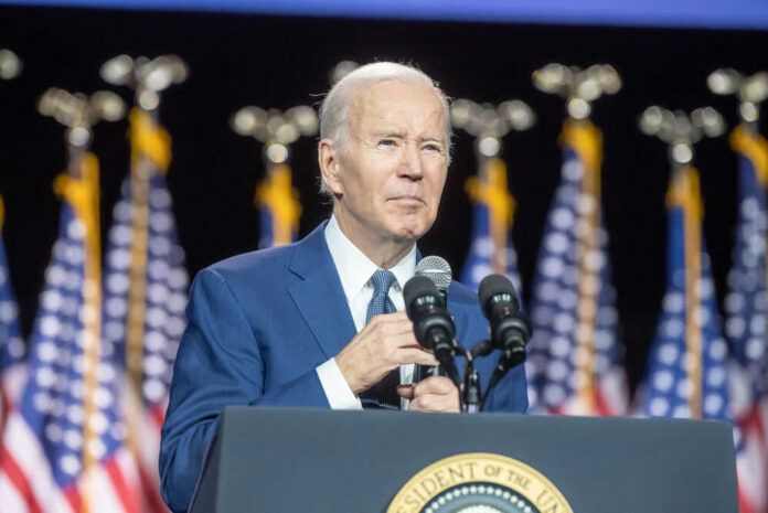 Man speaking at podium with flags behind him.