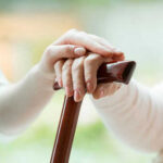 Hands resting on a wooden cane together
