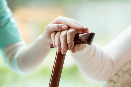 elderly-senior-living-740531920 Hands resting on a wooden cane together