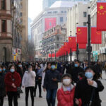 Crowded street with people wearing masks and flags