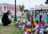 Police officer kneels at a memorial with flowers and tributes.