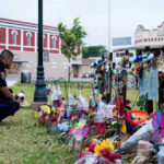 Police officer kneels at a memorial with flowers and tributes.