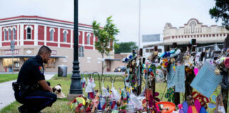Police officer kneels at a memorial with flowers and tributes.