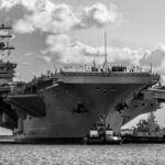 Large aircraft carrier being assisted by tugboats in the ocean