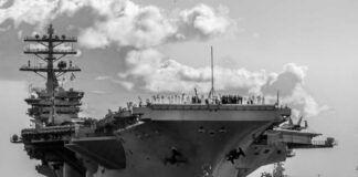 Large aircraft carrier being assisted by tugboats in the ocean
