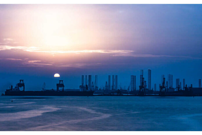 shutterstock_1264789975.jpg Silhouette of ships and cranes at an industrial harbor during sunset
