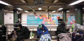 Individuals sitting on benches in a subway station, some covered with blankets