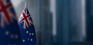 Australian flag displayed on a flagpole with a blurred city background