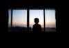 Silhouette of a child looking out a window at a sunset