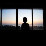 Silhouette of a child looking out a window at a sunset