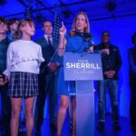 A female politician delivering a speech at a podium with supporters behind her