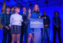 A female politician delivering a speech at a podium with supporters behind her