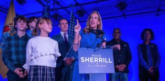 A female politician delivering a speech at a podium with supporters behind her