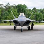 F-22 Raptor military aircraft on the tarmac with a crew member performing maintenance