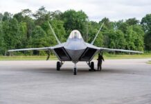 F-22 Raptor military aircraft on the tarmac with a crew member performing maintenance