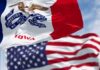 Iowa state flag in front of the American flag, both waving in the wind