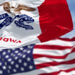 Iowa state flag in front of the American flag, both waving in the wind