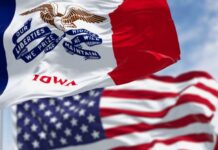 Iowa’s War Grief – National Politics Clash Iowa state flag in front of the American flag, both waving in the wind