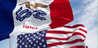 Iowa state flag in front of the American flag, both waving in the wind