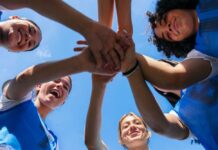 Group of female athletes joining hands in a circle under a blue sky