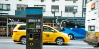 A parking meter on a city street with a yellow taxi passing by