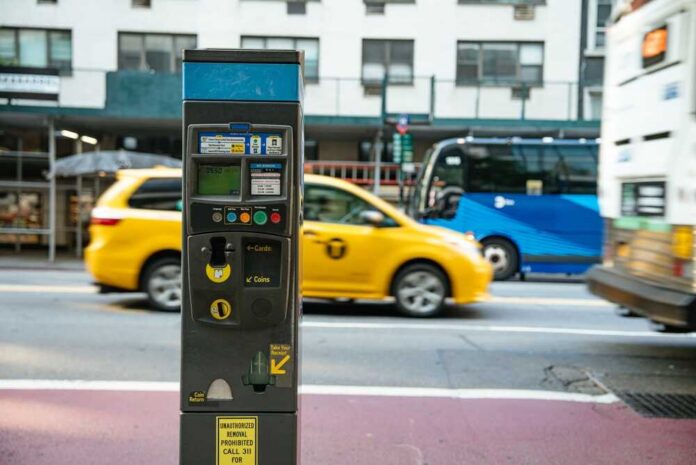 A parking meter on a city street with a yellow taxi passing by