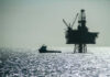 An offshore oil rig silhouetted against the shimmering sea with a small boat nearby