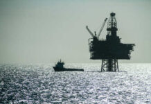 An offshore oil rig silhouetted against the shimmering sea with a small boat nearby