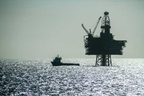 An offshore oil rig silhouetted against the shimmering sea with a small boat nearby