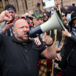 A man shouting into a megaphone during a protest with a crowd in the background