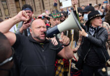 A man shouting into a megaphone during a protest with a crowd in the background