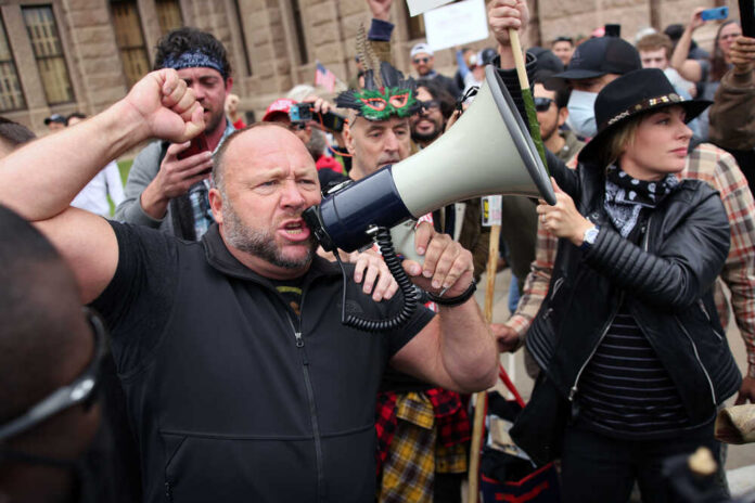 A man shouting into a megaphone during a protest with a crowd in the background