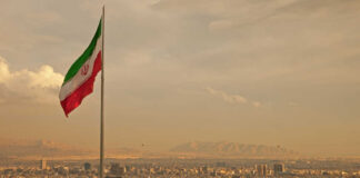 Iranian flag waving over a city skyline with mountains in the background