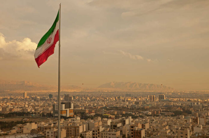 Iranian flag waving over a city skyline with mountains in the background