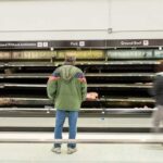 A man stands in front of empty meat shelves in a grocery store