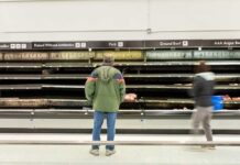 A man stands in front of empty meat shelves in a grocery store