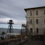 Alcatraz Revival: Bold Law-and-Order Move An old lighthouse next to a weathered building by the water under a cloudy sky