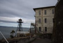 Alcatraz Revival: Bold Law-and-Order Move An old lighthouse next to a weathered building by the water under a cloudy sky