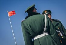 Two Chinese soldiers in uniform standing near the national flag