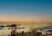 An oil rig in a desert landscape under a colorful sky