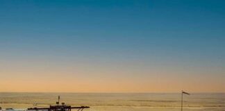 An oil rig in a desert landscape under a colorful sky