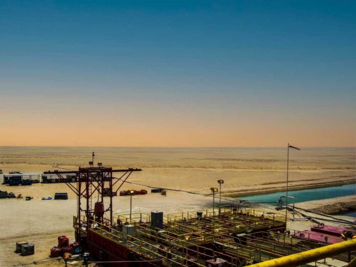 An oil rig in a desert landscape under a colorful sky