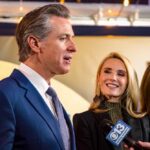 A man speaking at a public event with two women smiling nearby