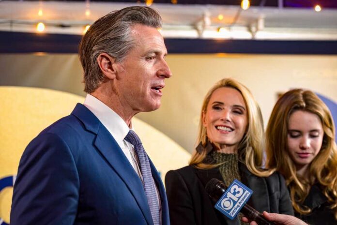A man speaking at a public event with two women smiling nearby