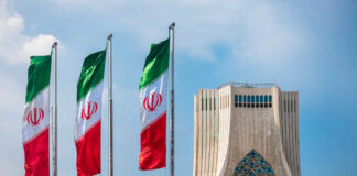 Three Iranian flags in front of the Azadi Tower against a blue sky