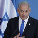 Man speaking in front of Israeli flag backdrop