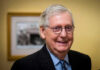 Smiling man in suit with round glasses indoors.